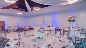 A banquet hall with round tables set for dining, white drapes, and a floral centerpiece. - Hampton Inn & Suites Boston/Stoughton (Stoughton)