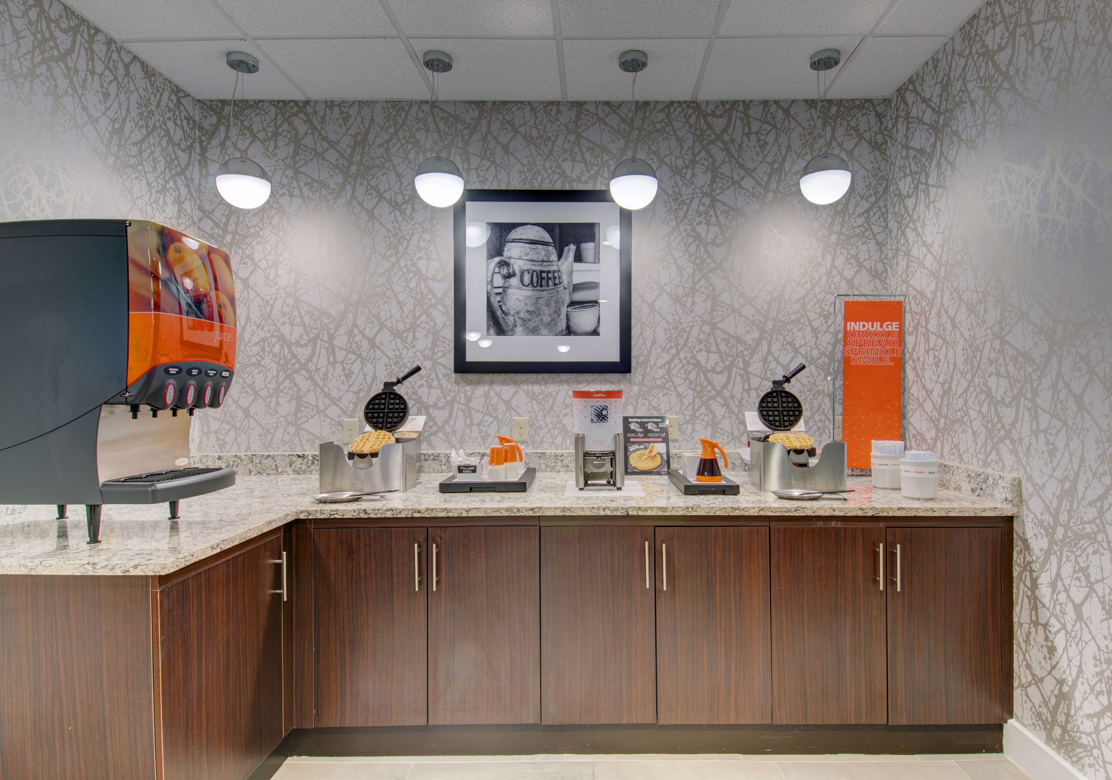 A coffee station with multiple coffee makers and a framed coffee-themed artwork on the wall.