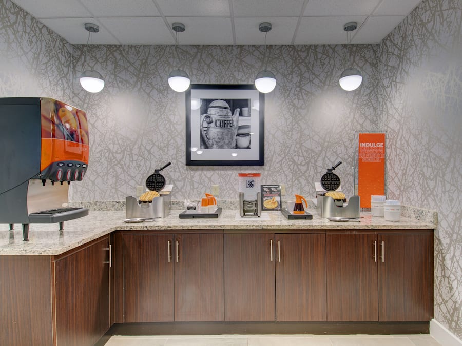 A coffee station with multiple coffee makers and a framed coffee-themed artwork on the wall.