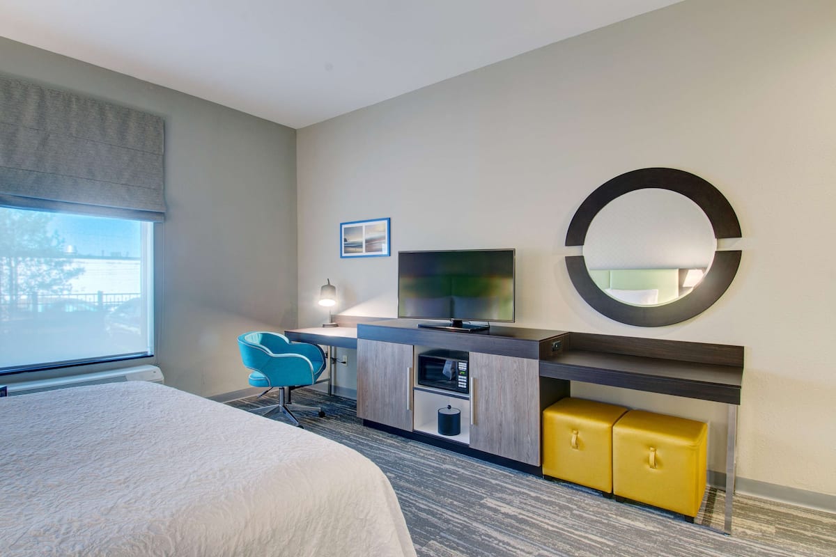 Une chambre d’hôtel avec un lit, un bureau avec une télévision, un four à micro-ondes et un meuble de rangement jaune.