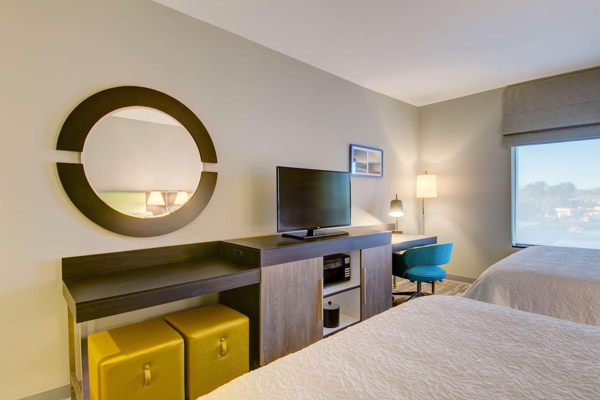 Une chambre d’hôtel avec un lit, une télévision, un bureau avec une lampe, une chaise et une grande fenêtre.