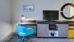 A hotel room with a desk, a chair, a television, a mirror, and a framed picture on the wall. - Hampton Inn & Suites Boston/Stoughton (Stoughton)