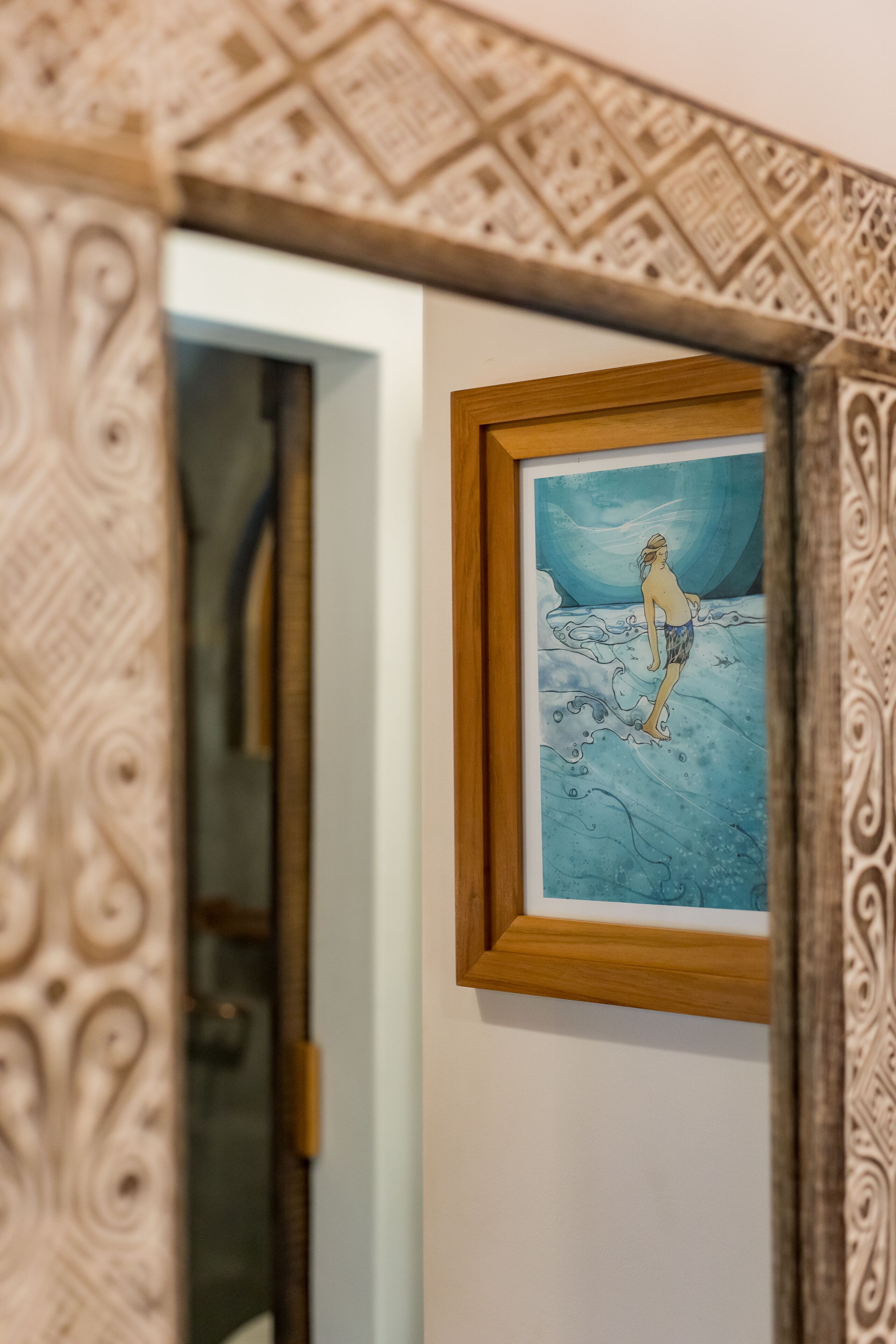 A framed artwork of a person standing on a beach with waves, mounted on a wall with a patterned border.
