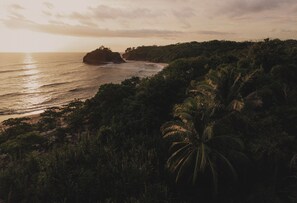 A coastal landscape with a beach, dense vegetation, and a prominent rock formation. - The Nomadic Hotel (Nosara)