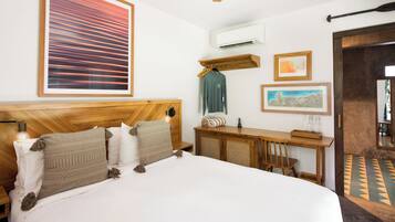 Ein Hotelzimmer mit Holz-Kopfteil, einem Bett mit weißen Leinentüchern, einem Schreibtisch mit Stuhl und einem großen, abstrakten Gemälde an der Wand.