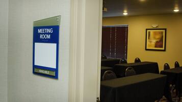 A meeting room with tables and chairs, a sign indicating availability, and a window with blinds.