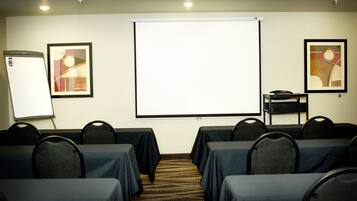 A conference room with tables and chairs, a projector screen, and two framed artworks on the walls.