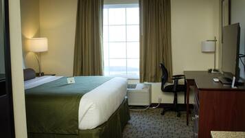Una habitación de hotel con cama, escritorio, silla y ventana con cortinas.