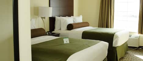 Habitación de hotel con dos camas, una mesita de noche, una lámpara y una ventana con cortinas.
