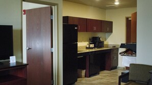A compact kitchen with wooden cabinets, a refrigerator, a coffee maker, and a chair. - Cobblestone Inn & Suites – Soda Springs (Soda Springs)