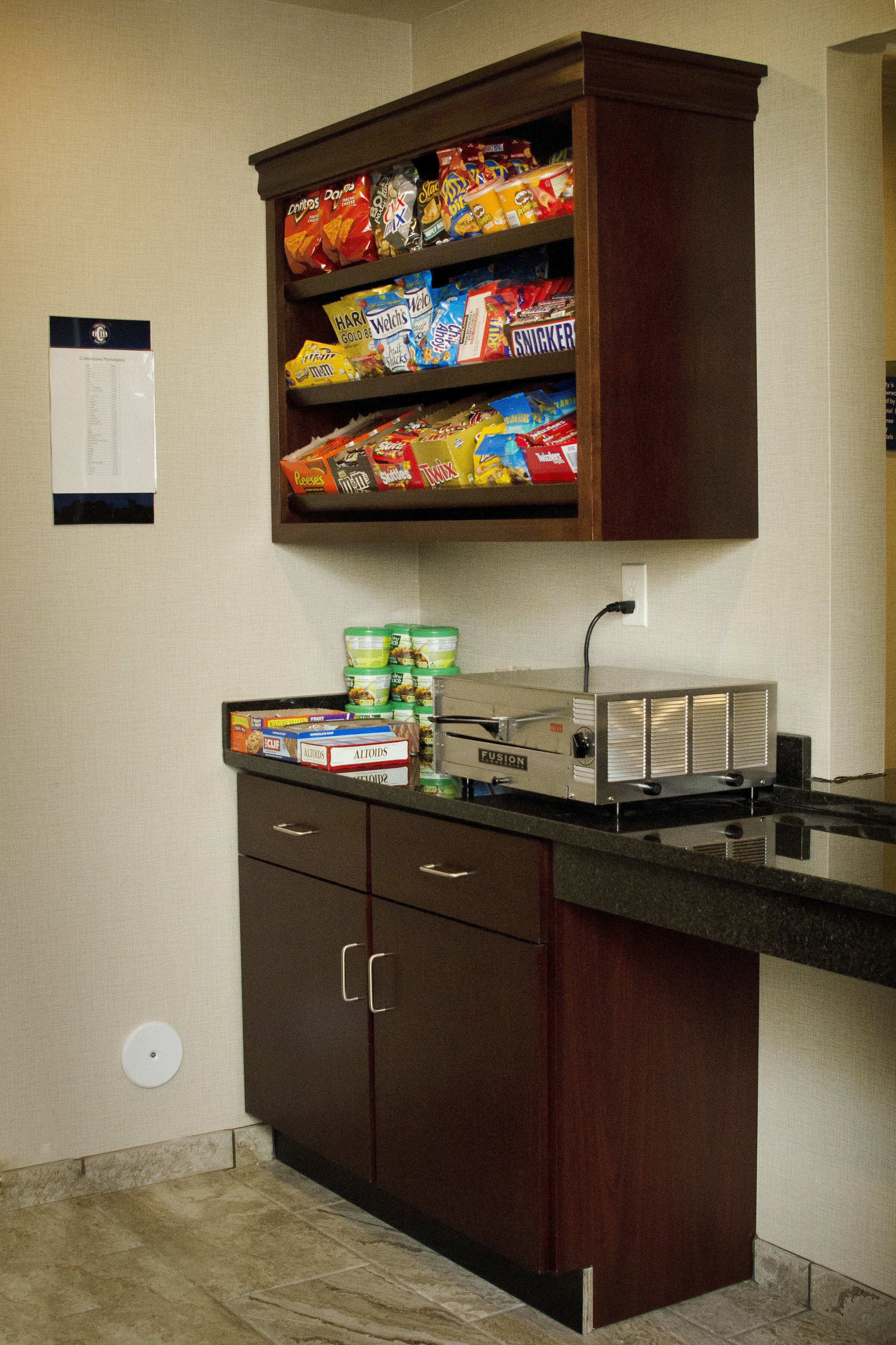 A kitchenette with a built-in microwave, a coffee maker, and a shelf stocked with snacks.