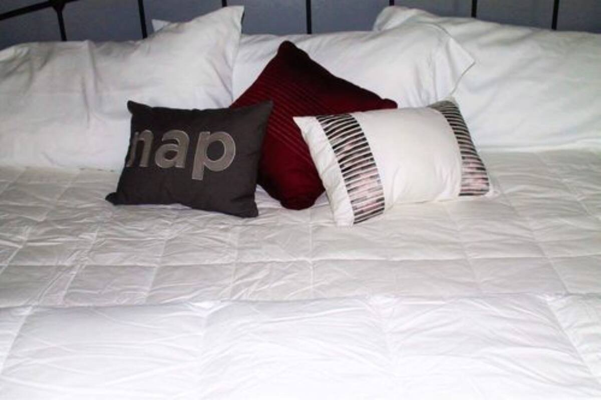 A bed with white bedding and three pillows, one with a visible word on it.