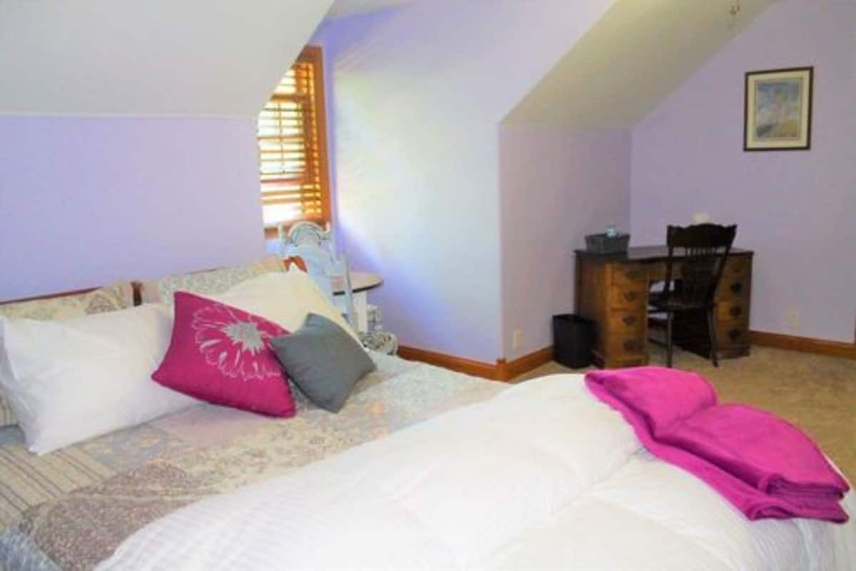A bedroom with a bed, pillows, a desk, and a chair.