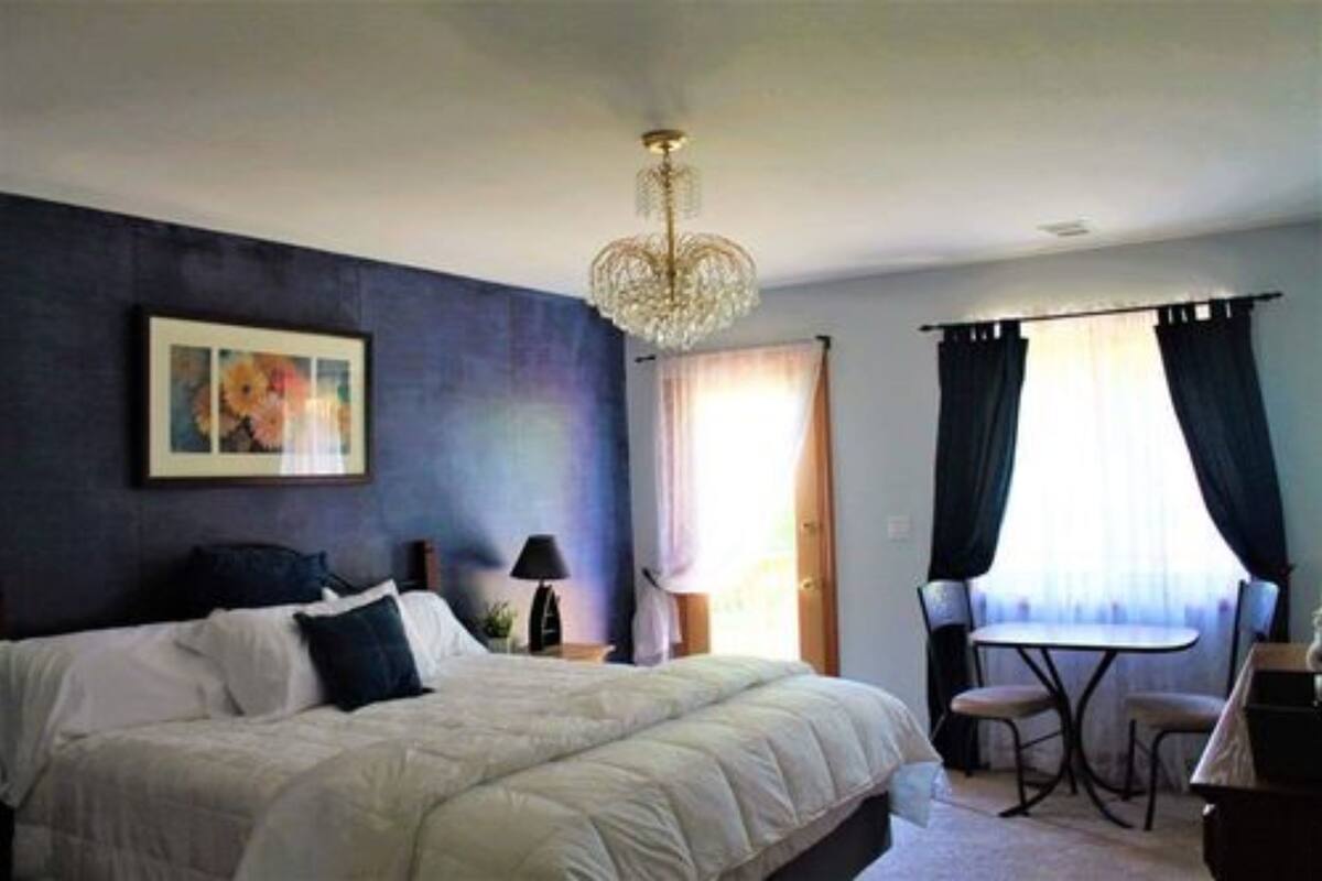 A bedroom with a large bed, a chandelier, a desk with two chairs, and a window with curtains.