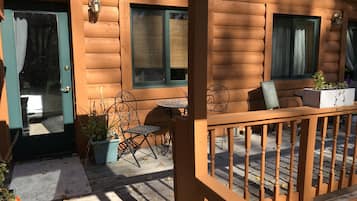 A wooden cabin with a porch, a table, chairs, and potted plants.