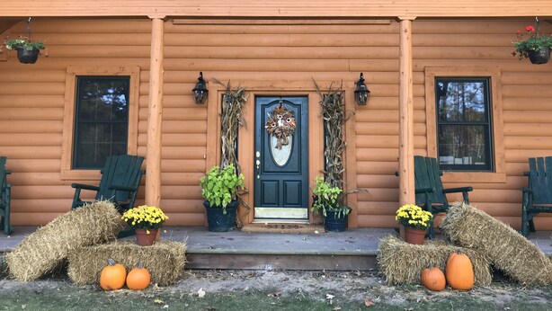 A log cabin with a front porch, two windows, a door with a wreath, and potted plants. - Oak Creek Lodge (Bannister)