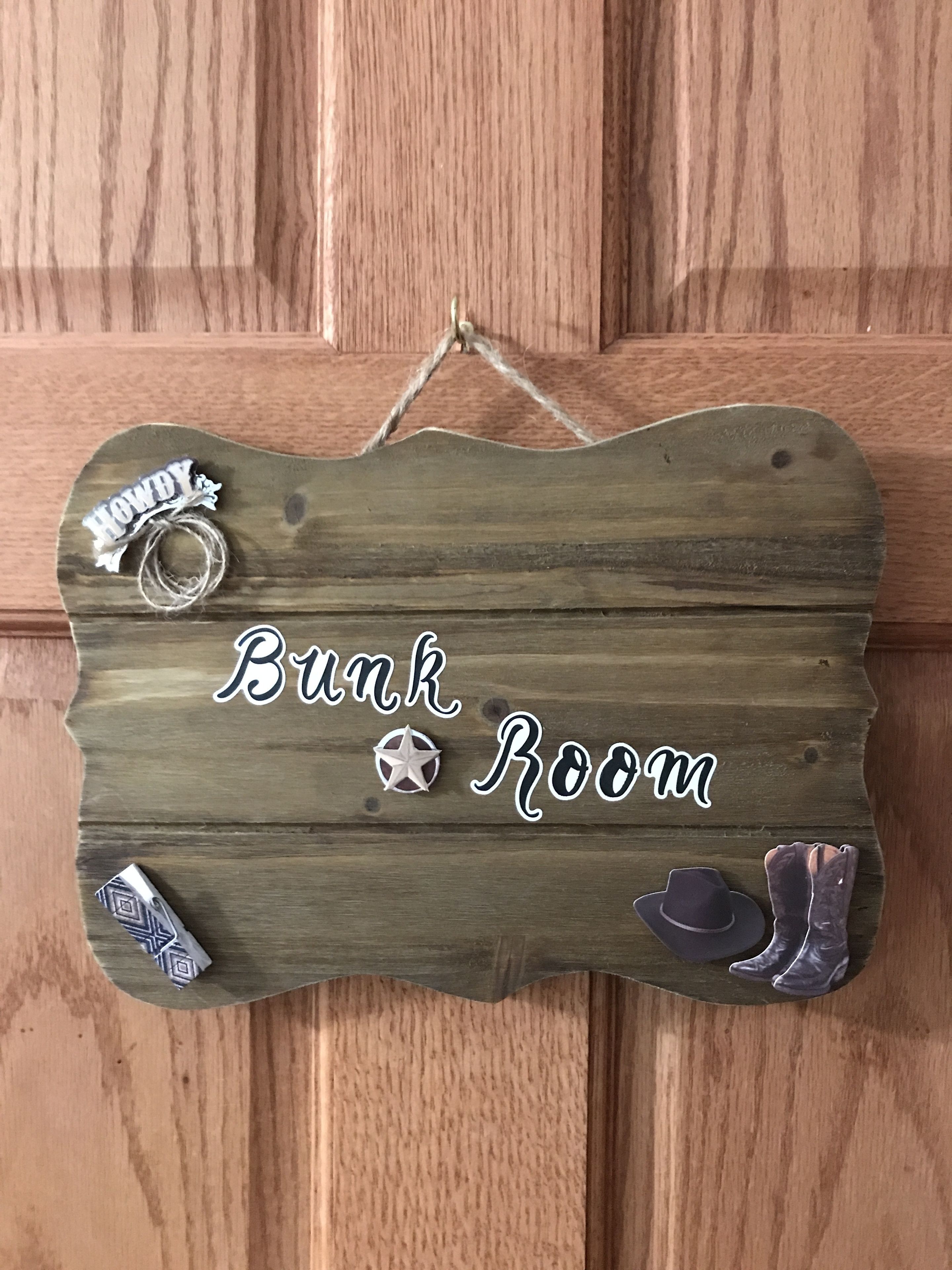 A wooden sign with the text "Bunk Room" and decorative elements like a star, a rope, and a hat.