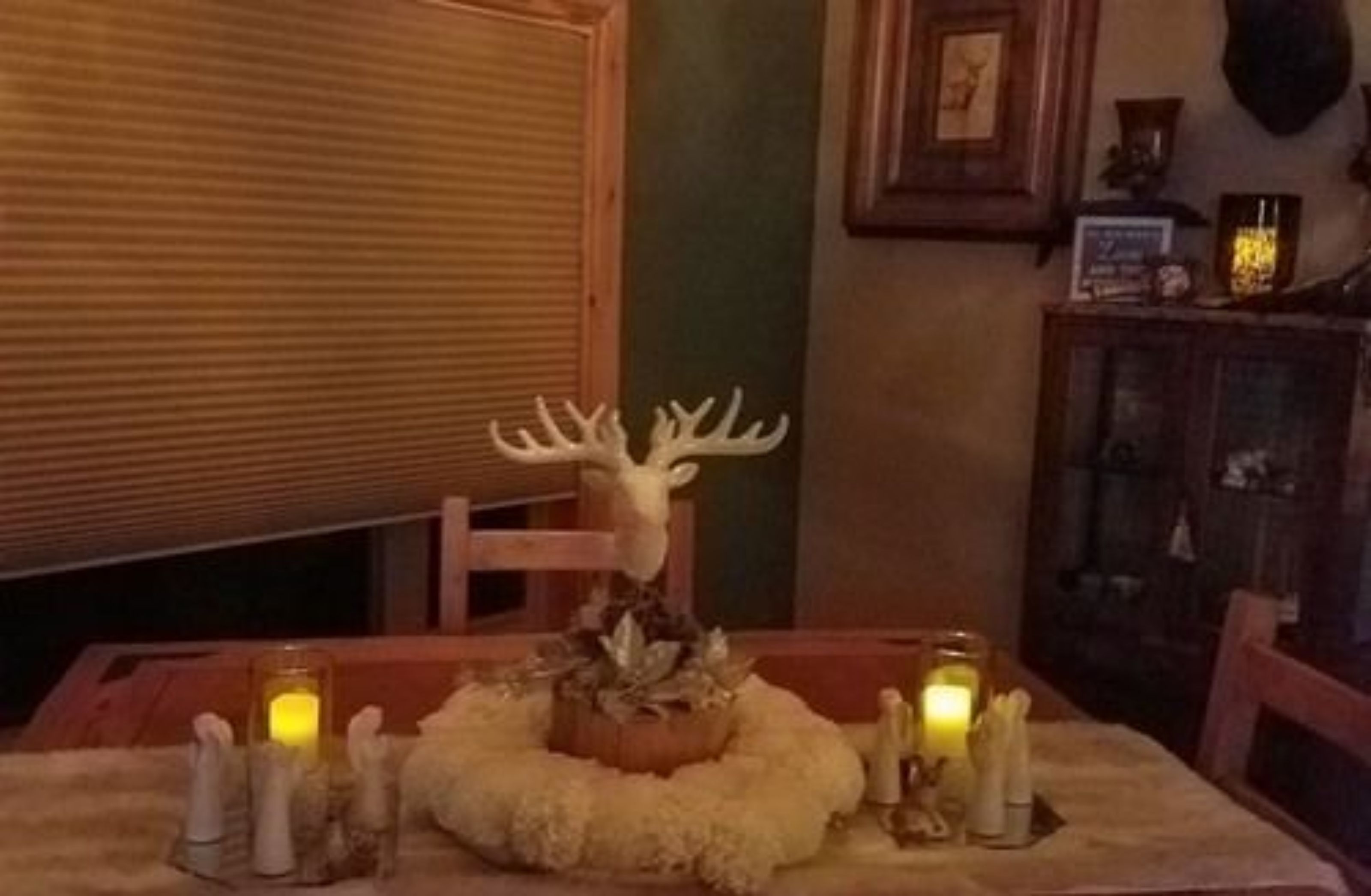 A dining table with a deer head centerpiece, candles, and a rustic setting.