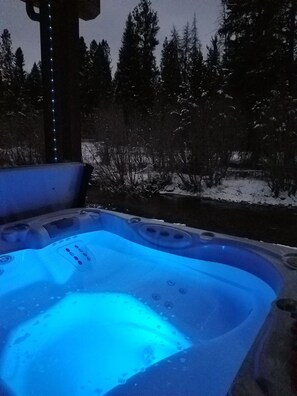 A hot tub with a blue light, surrounded by snow-covered ground and trees.