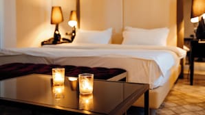 A hotel room with a neatly made bed, two bedside lamps, and a glass table with candles. - Senator Hotel (Tirana)