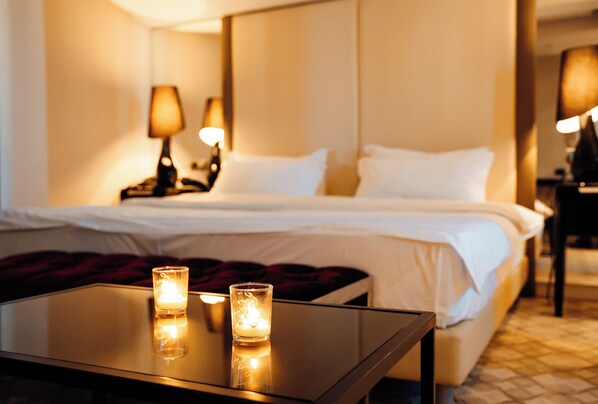 Una habitación de hotel con una cama bien hecha, dos lámparas de noche y una mesita de vidrio con velas.