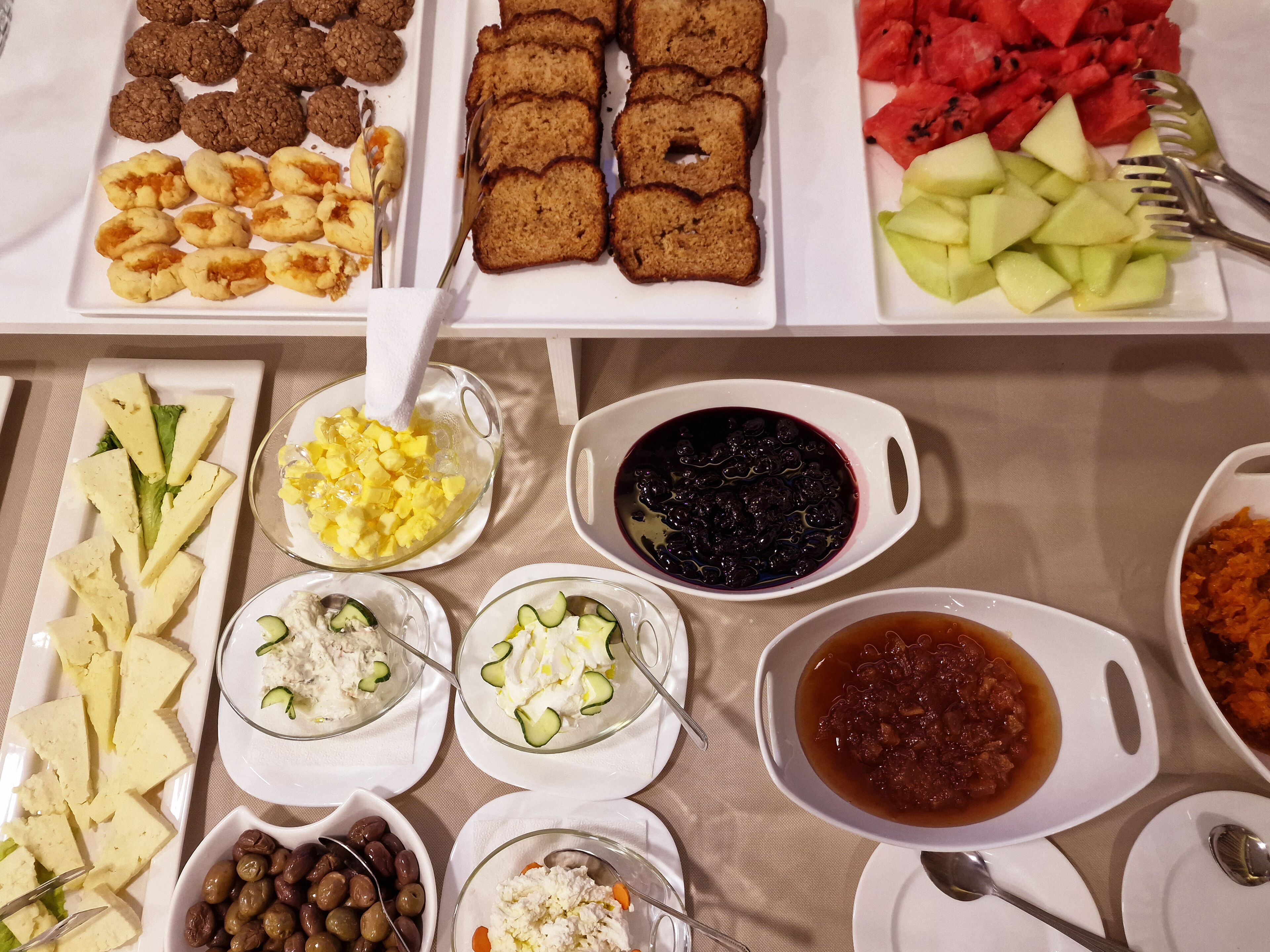 A variety of food items including cookies, bread, watermelon, and several types of dips and salads.