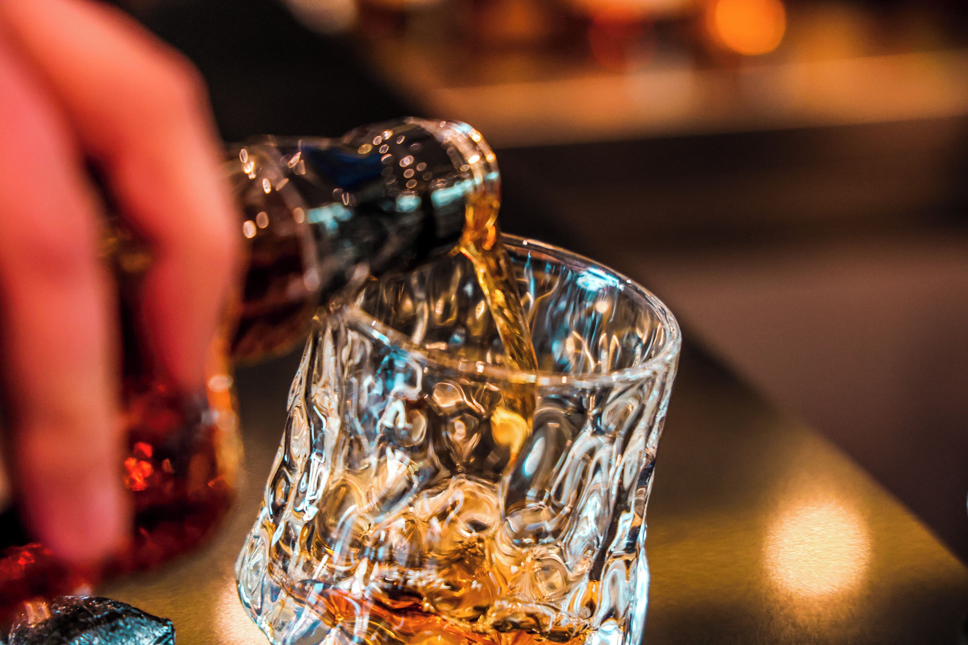 A close-up of a hand pouring a golden liquid into a textured glass.