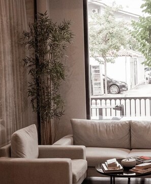 A living room with a sofa, a coffee table with books and a bowl, and a large bamboo plant. - Senator Hotel (Tirana)