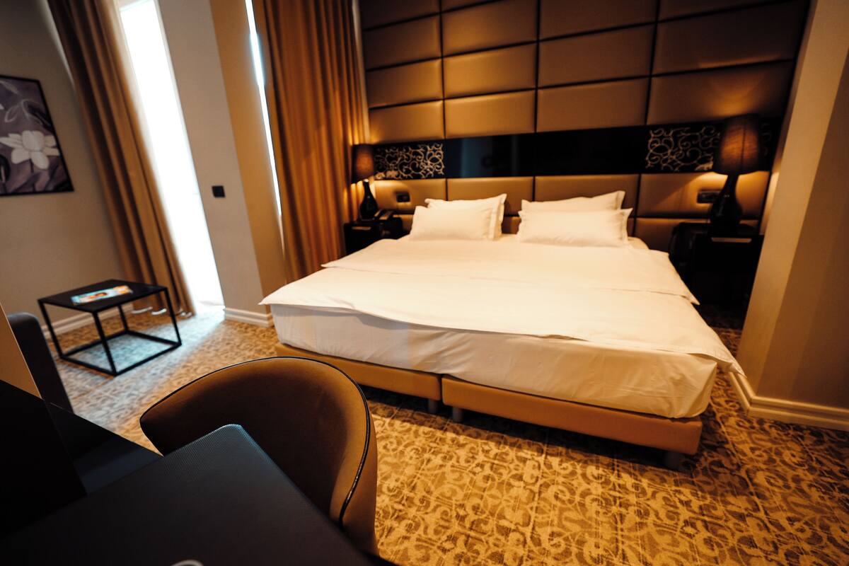 Una habitación de hotel con una cama grande, dos mesitas de noche, una silla y una pequeña mesa.