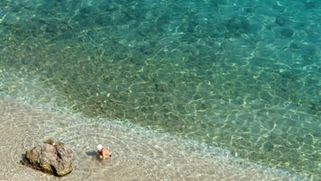Ein freier Blick auf einen Strand mit einer Person im Wasser und einem großen Felsen am Ufer.
