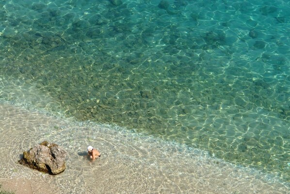 A clear view of a beach with a person in the water and a large rock on the shore.