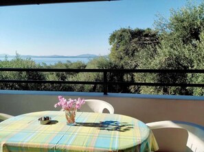 A table with a plaid tablecloth, a vase with pink flowers, and a metal ashtray on a balcony overlooking a body of water and trees. - Villa Stefanos Apartments by Hotelius (Corfu)