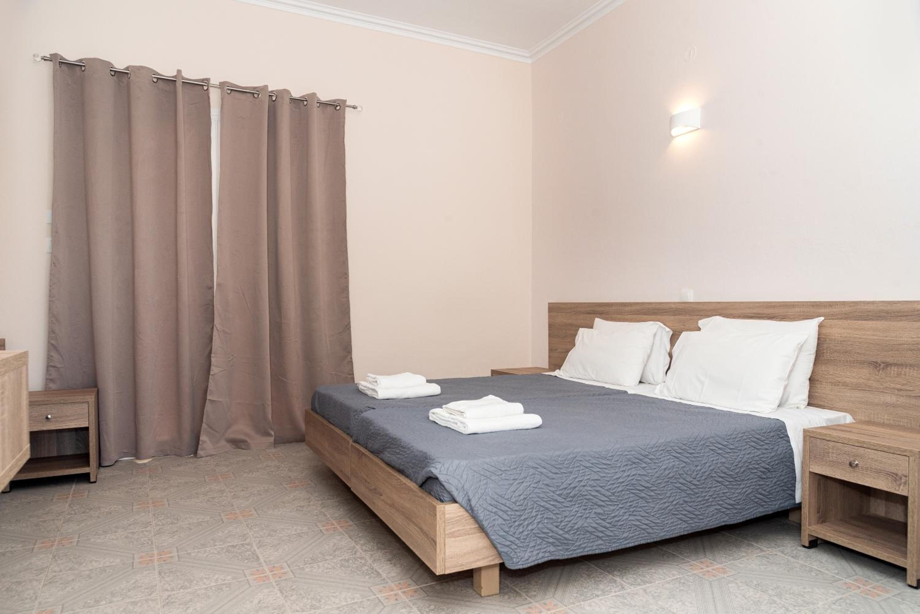 A bedroom with a bed, two bedside tables, a nightstand, a wall-mounted light, and a curtain.