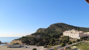Uma estrada costeira com uma praia de um lado e uma colina com edifícios do outro.