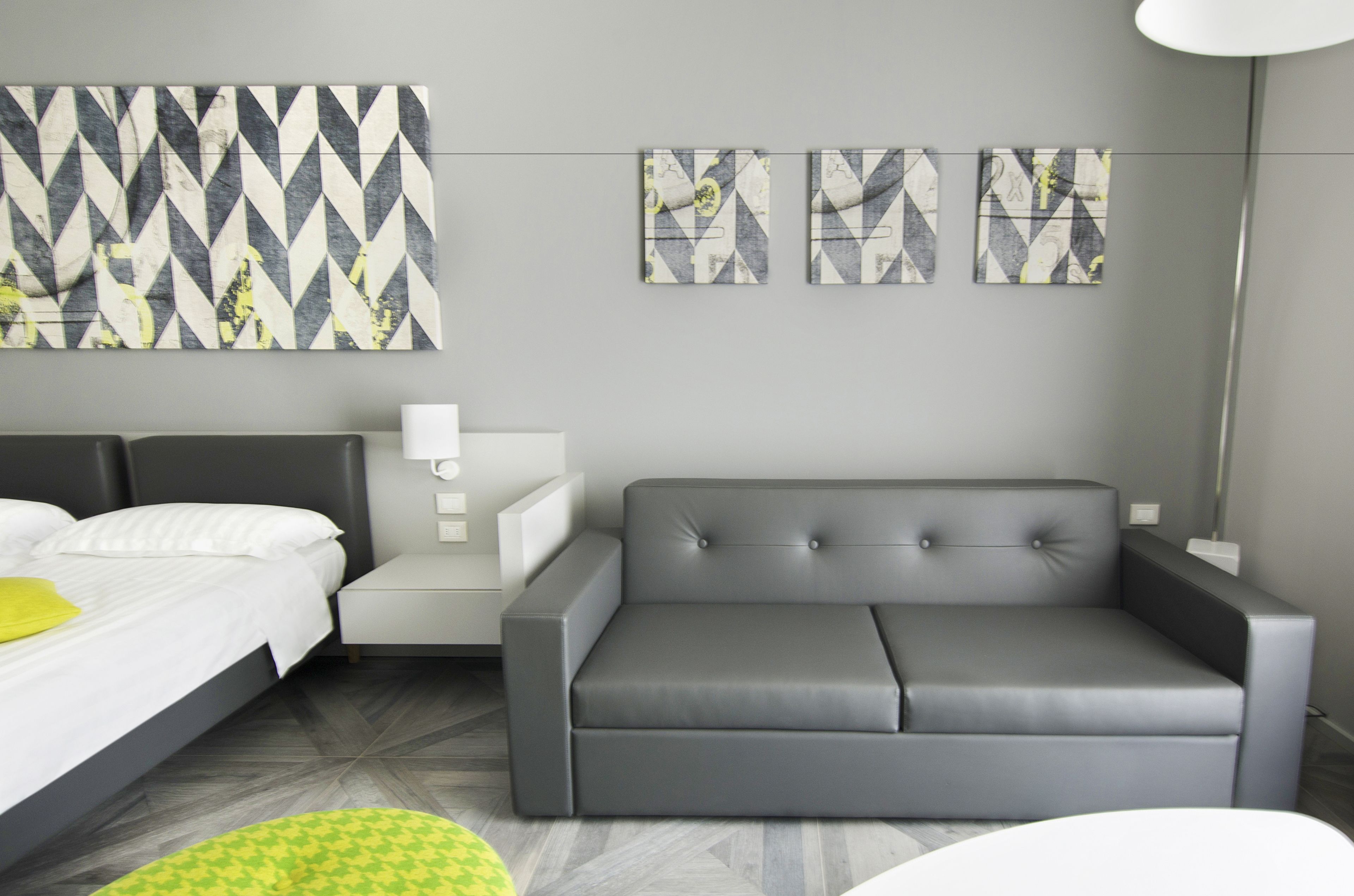 A modern hotel room with a bed, a grey sofa, and a nightstand.