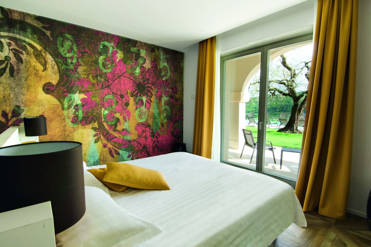 A hotel room with a large bed, a view of the outdoors, and a colorful mural on the wall.