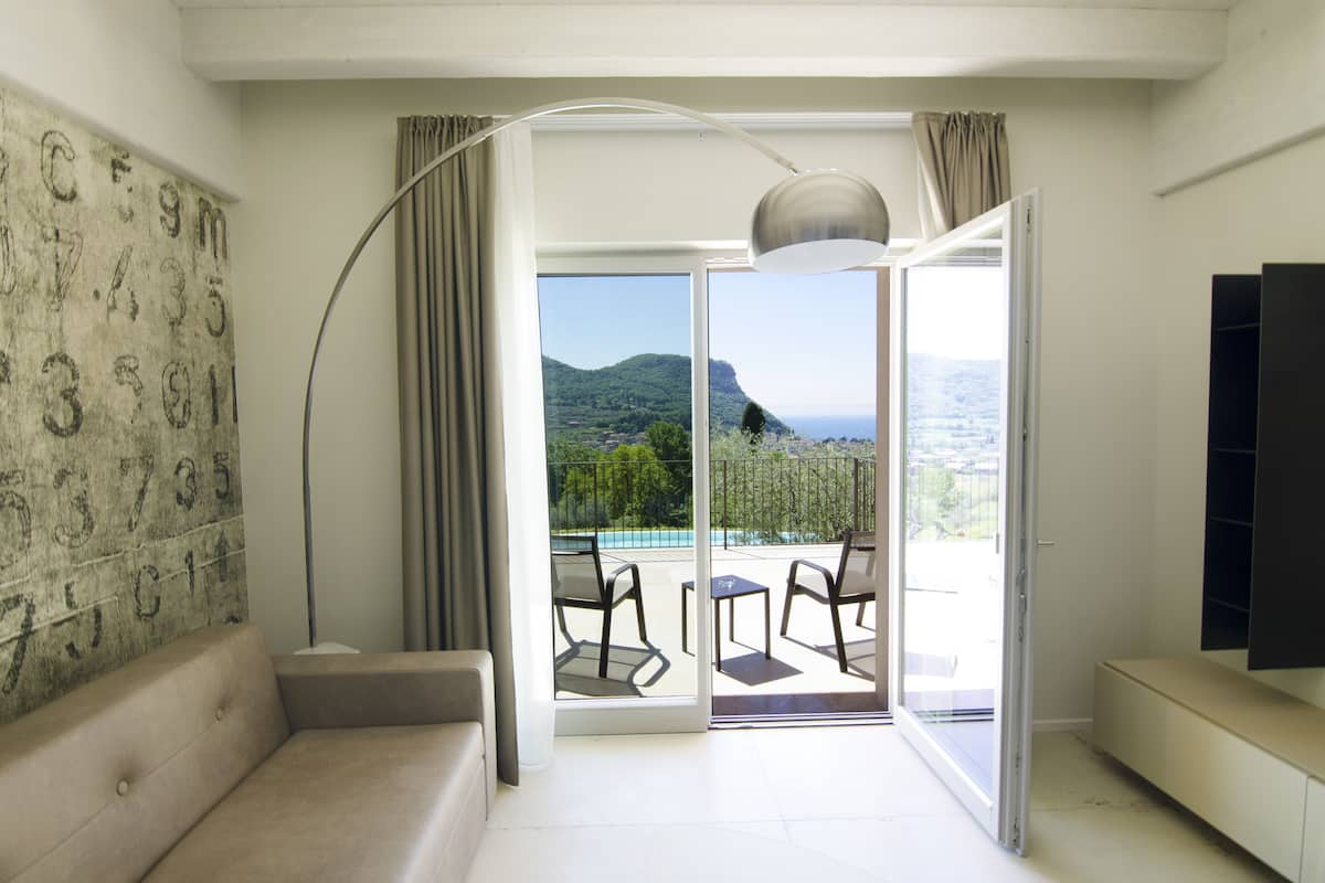 A modern living room with a sofa, a large floor lamp, and a sliding glass door leading to a balcony with a pool view.