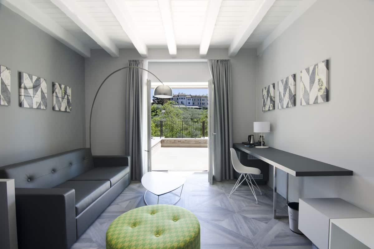 A modern room with a sofa, a dining table, a desk, and a view of greenery outside.