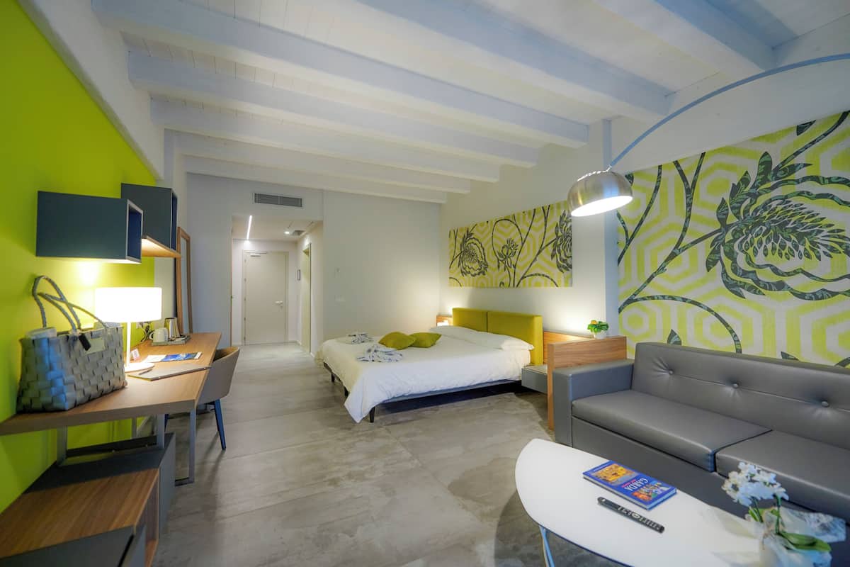 A modern hotel room with a bed, a desk, a sofa, and a large floral wall mural.