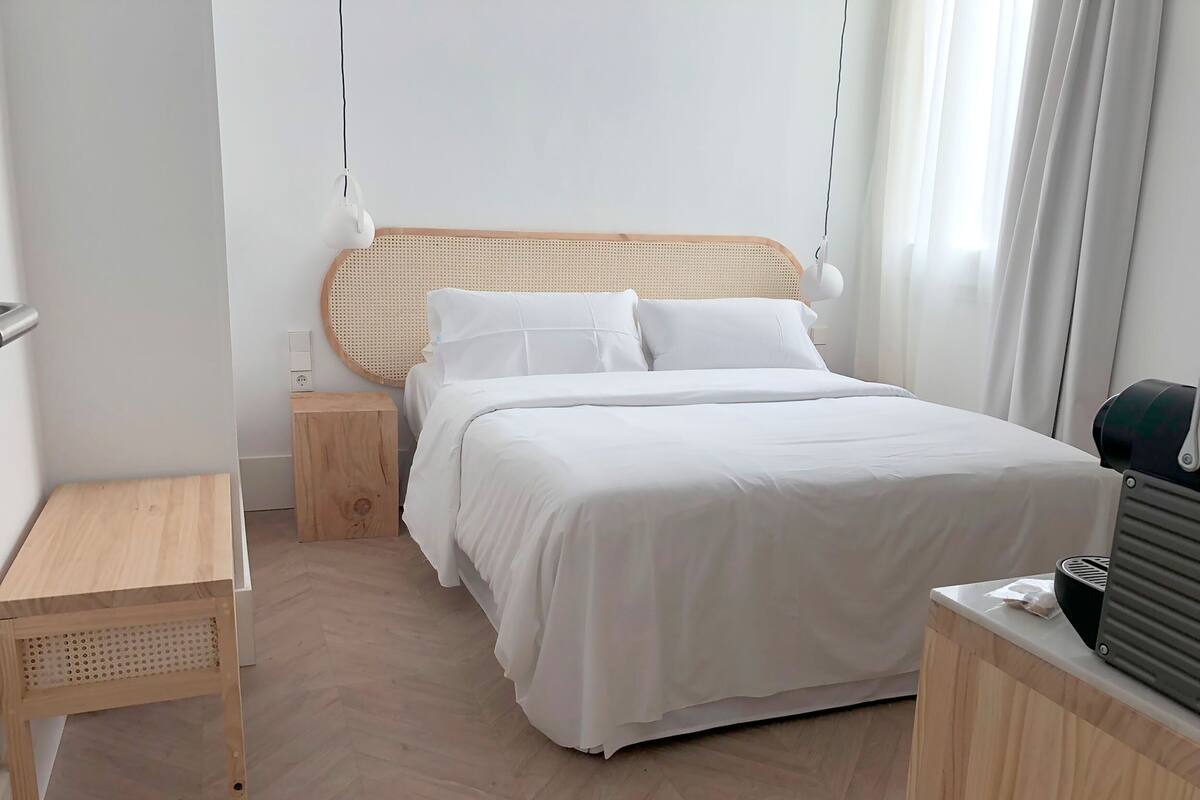 Une chambre d’hôtel bien rangée, avec un lit, une table de chevet et une petite table de nuit en bois.