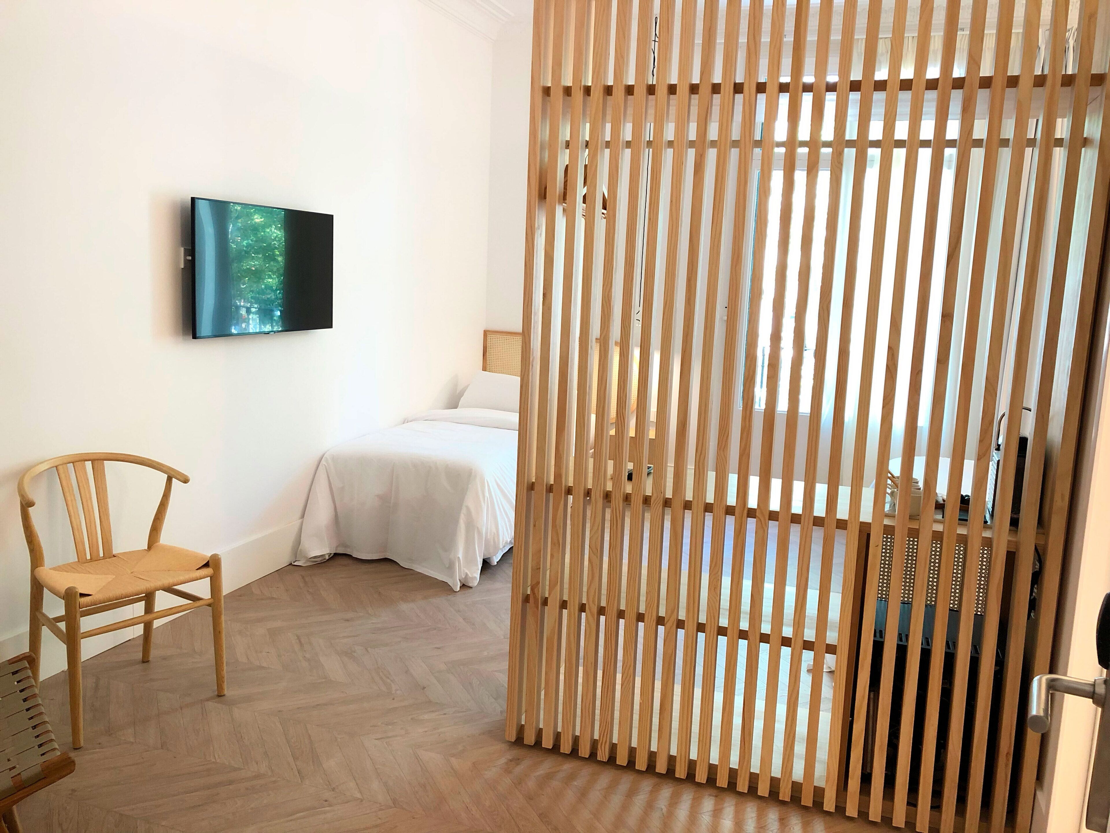 Una habitación con cama, una silla, televisión montada en la pared y un separador de madera.