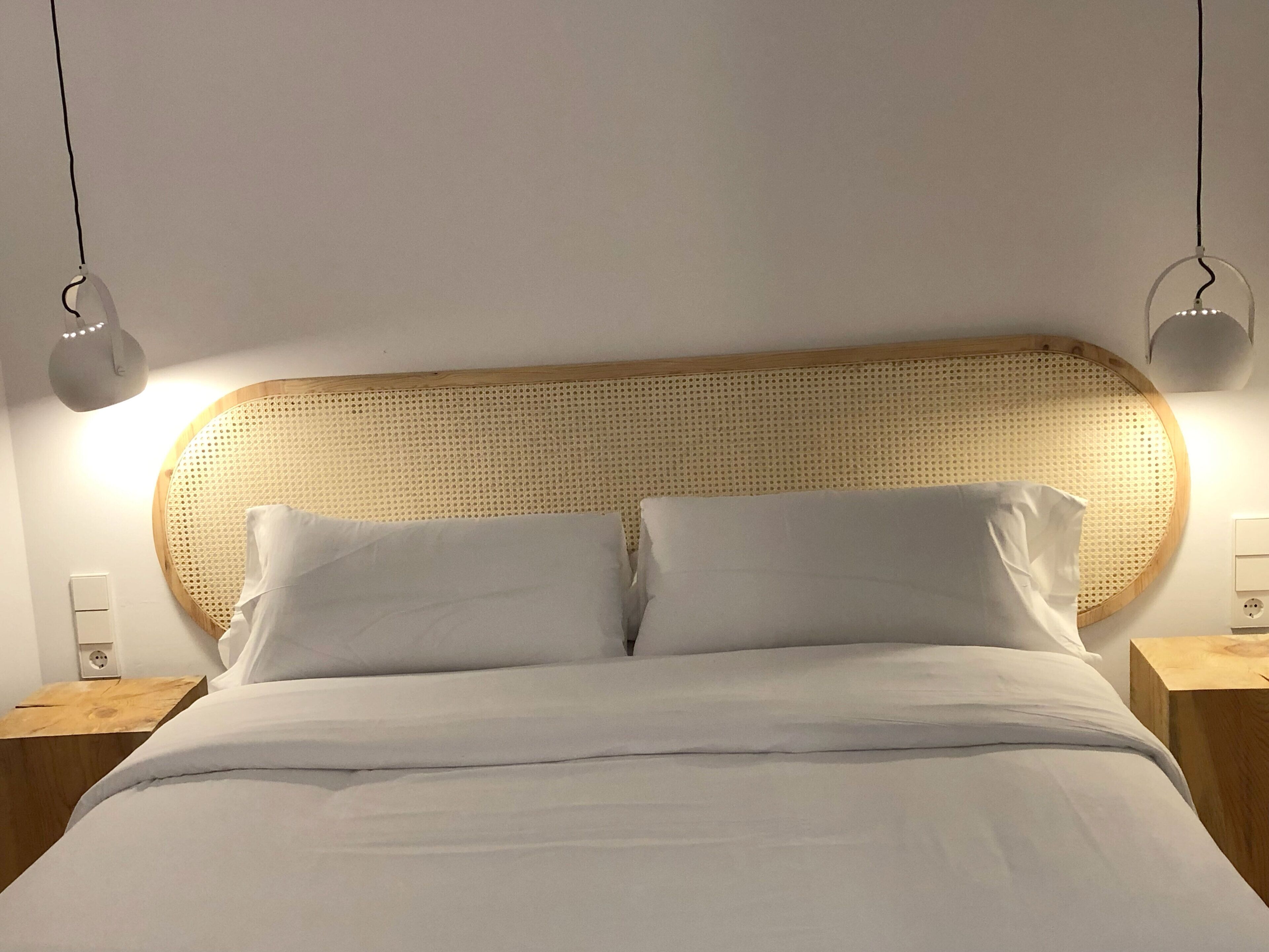 A bed with a woven headboard, two bedside tables, and wall-mounted lamps.