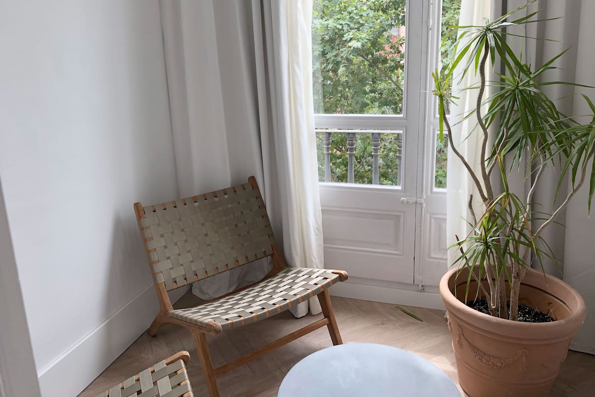 Une pièce d’angle avec un fauteuil en osier, une plante en pot et une fenêtre avec des rideaux.