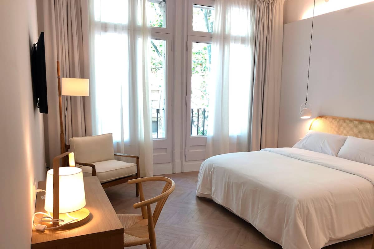 Une chambre d’hôtel avec un lit, un bureau avec une lampe, une chaise et un téléviseur fixé au mur.