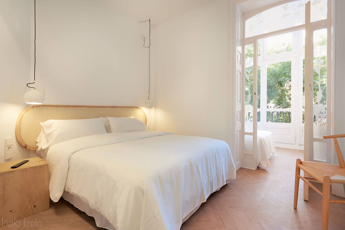 Une chambre à coucher avec un grand lit, des tables de chevet, une chaise et une fenêtre donnant sur un paysage verdoyant.
