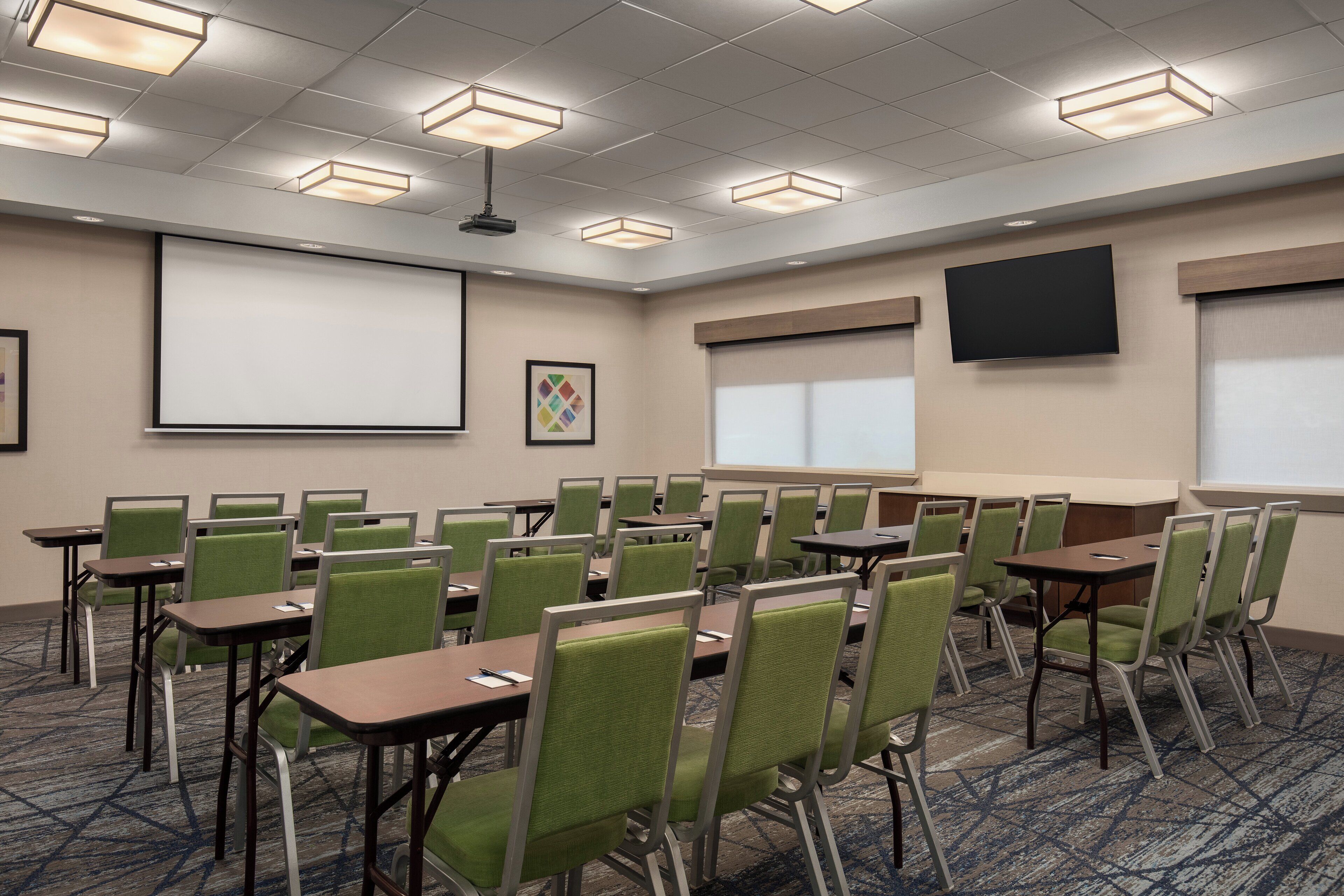 A conference room with green chairs, tables, a projector screen, and a large screen on the wall.