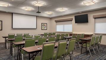 A conference room with green chairs, tables, a projector screen, and a large screen on the wall.