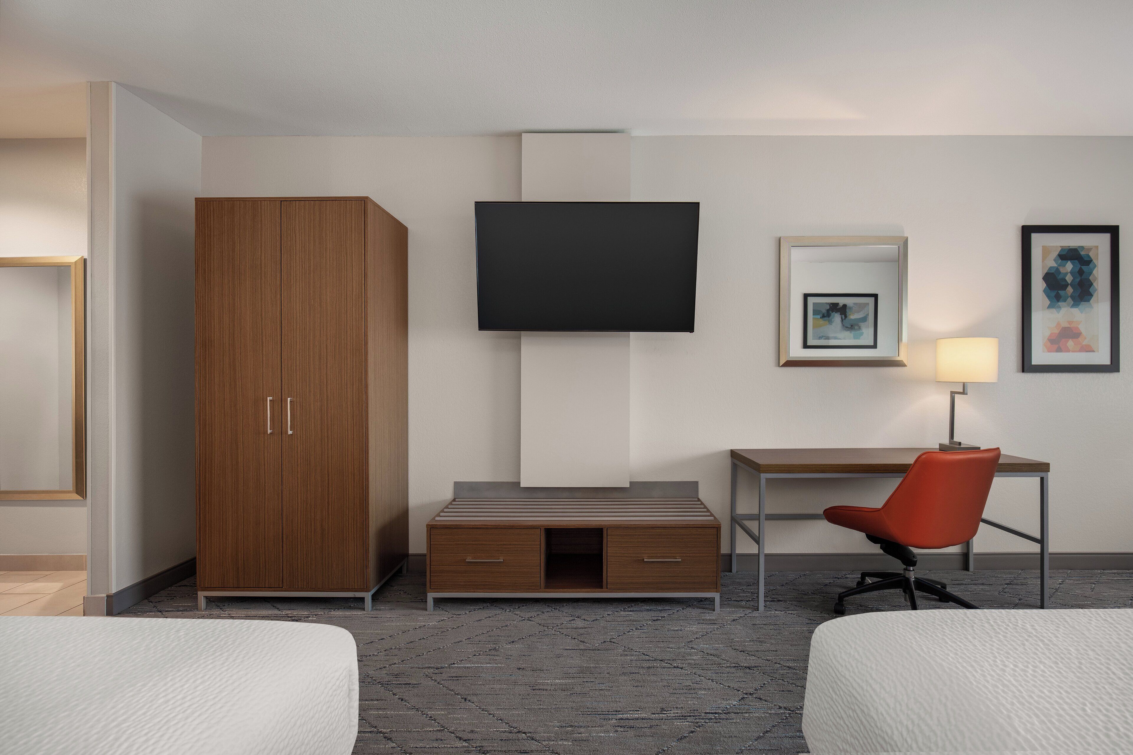 Une chambre d’hôtel comprenant un lit, une armoire en bois, un bureau avec une chaise, un téléviseur à écran plat et des œuvres d’art accrochées au mur.