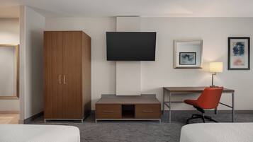 Une chambre d’hôtel comprenant un lit, une armoire en bois, un bureau avec une chaise, un téléviseur à écran plat et des œuvres d’art accrochées au mur.