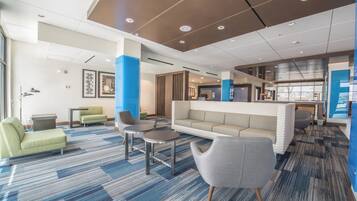 Un hall d’hôtel moderne, doté d’espaces aménagés avec des sièges, d’un comptoir de réception et offrant une vue sur l’extérieur.